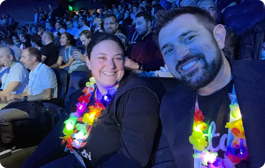 Two team members wearing light-up leis in the crowd at a conference keynote