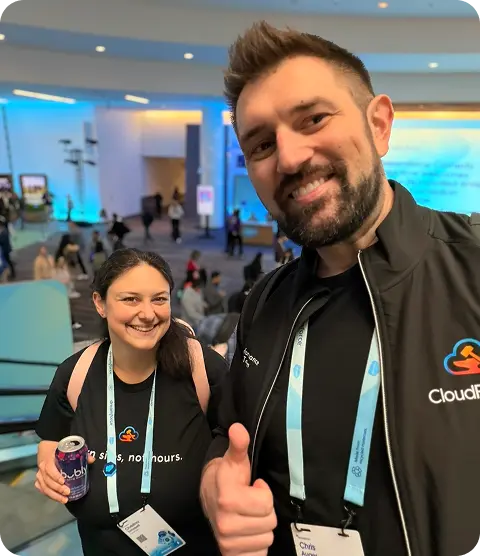 Two team members in CloudForged shirts at a Salesforce conference, one giving a thumbs-up