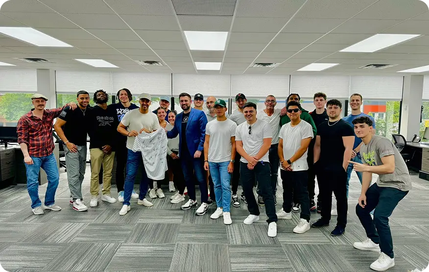 A big group photo of the team in an office, one person holding up a pinstriped baseball jersey
