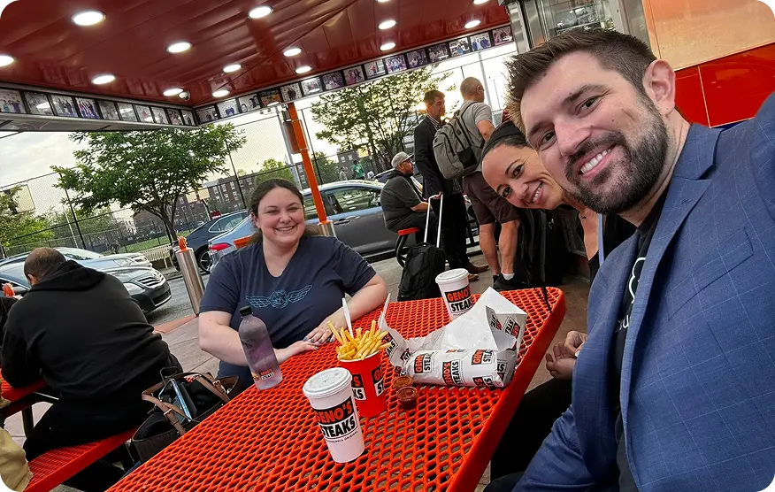 Team members sharing cheesesteaks at an outdoor table