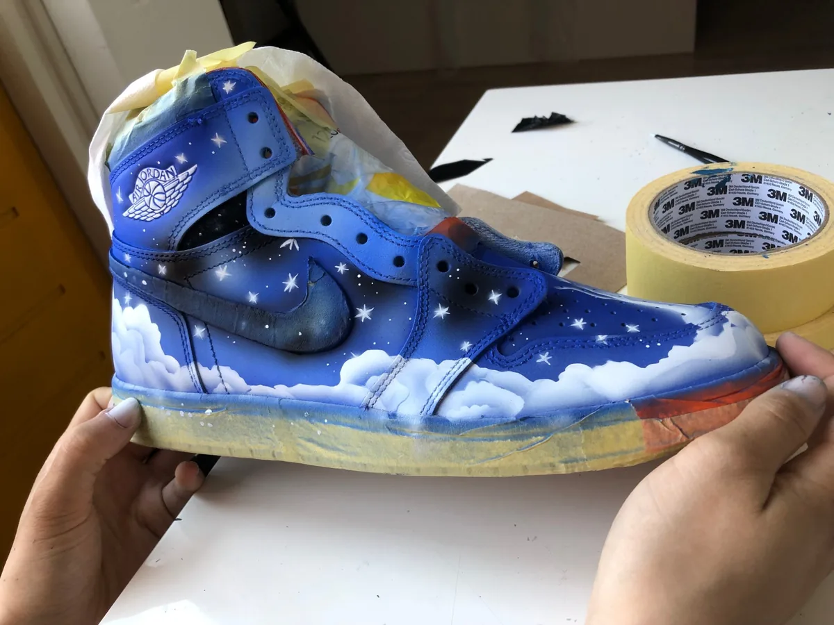 The painted shoe in the studio, sole still taped, stars dotted across the blue