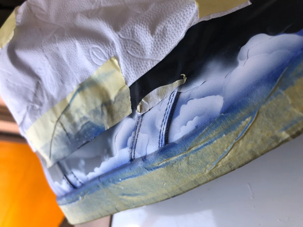 A shoe masked with tape and tissue, the clouds airbrushed layer by layer